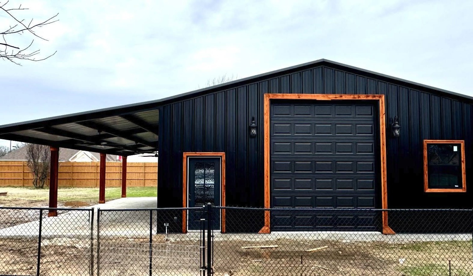 Black metal shop with cedar trimmed entry and a lean to carport