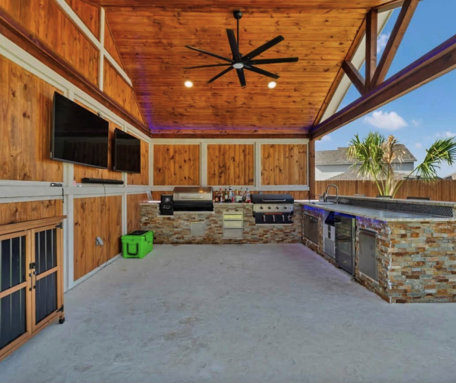 Outdoor kitchen under a cedar ceiling with televisions and grill
