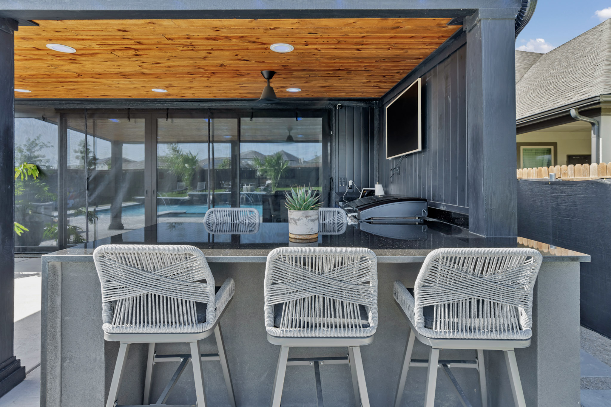 Poolside bar with a stone counter and rope bar stools under a cedar ceiling