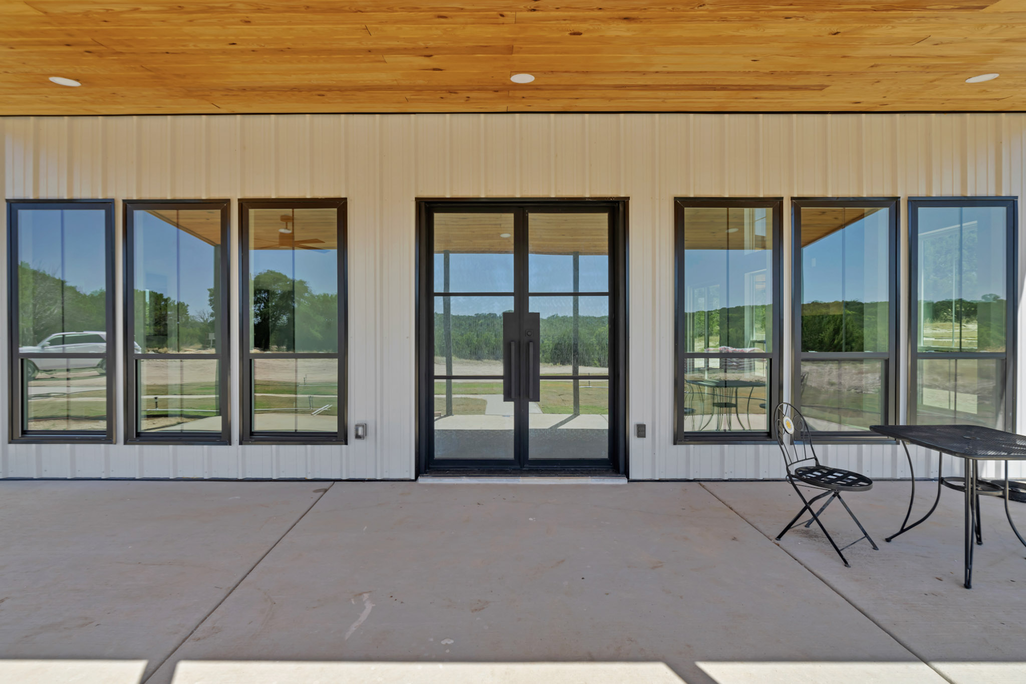 Covered porch with a cedar ceiling, black windows and an iron double entry door